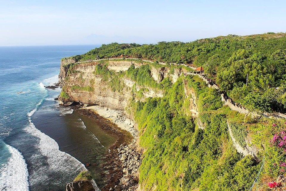 Uluwatu cliff path with orange-roofed pavilions, pink bougainvillea in the corner