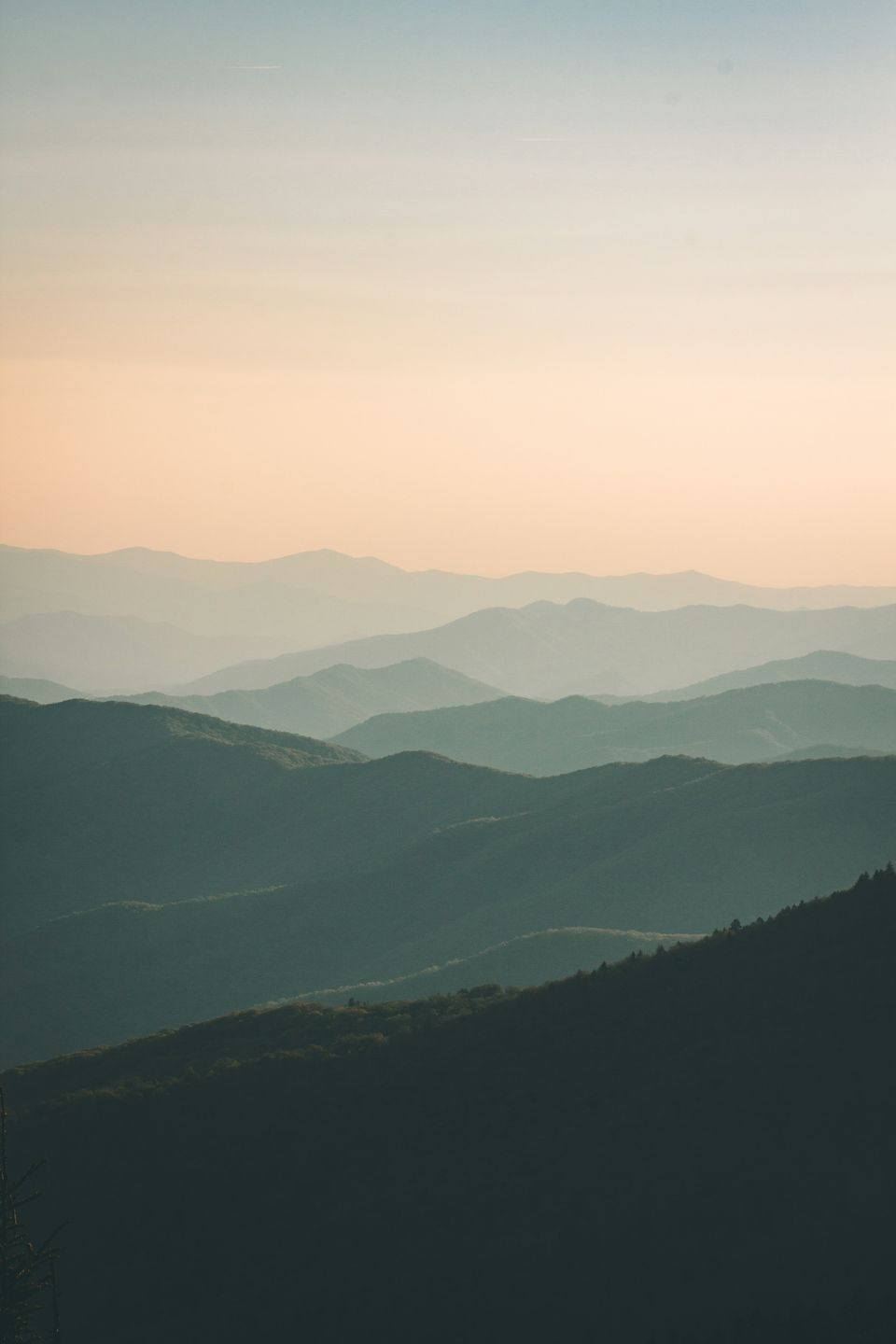 Layered misty mountain ridges under a soft pale sky