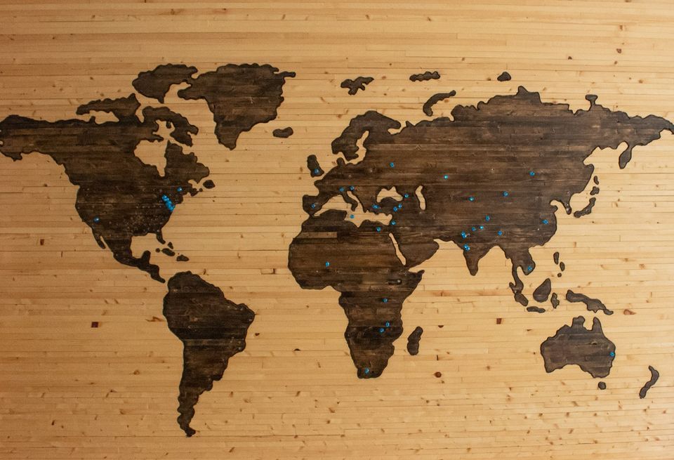 A wooden world map on a wall, marked with pins
